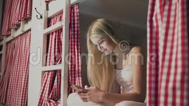 年轻漂亮的女人坐在<strong>宿舍</strong>的床<strong>上</strong>，用智能手机