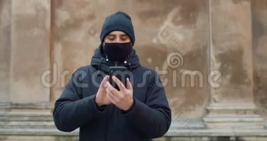 人行走和使用智能手机在社交网络中交流的正面视图。 穿着黑棉衣服的男人