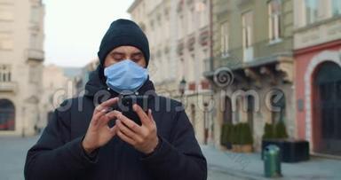 一个人站着的时候戴着医用口罩的年轻人用智能手机。 戴着防护面罩的人看着