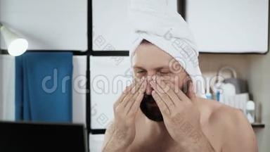 男人脸上涂奶油。 一个满脸胡须的白种人，头上戴着毛巾，用皱纹霜保湿