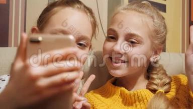 两个青少年女孩显示胜利标志为移动自拍。 少女们微笑着摆姿势准备手机拍照