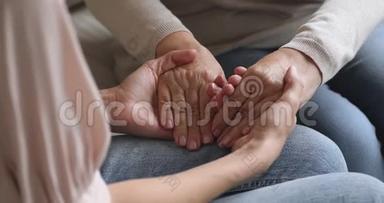 特写年轻女子牵着皱纹的老退休母亲的手。