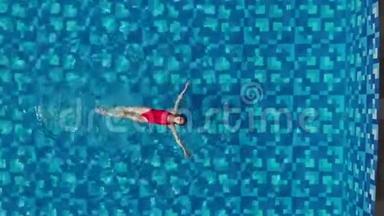 美丽的女士，穿着红色比基尼，背部游泳，在蓝色游泳池放松。 假期概念。 空中小牛肉