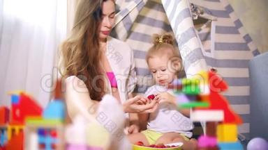 美丽的孕妇和她的小宝宝在玩具帐篷里吃树莓