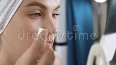 女孩在用遮瑕膏。 浴室里漂亮的年轻女子照镜子，在她身上涂上海绵遮瑕膏