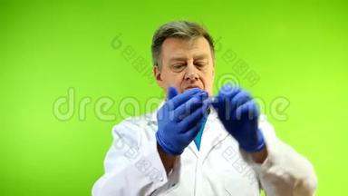 穿着白大褂的严肃的高级成人医生脱下了他的橡胶手套，这种手套外界感染的保护。 绿色