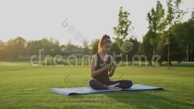 一个年轻的女孩<strong>在做瑜伽</strong>后坐<strong>在</strong>绿草上，用手机。