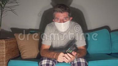 Covid-19病毒恐慌锁定-悲伤和焦虑的男人戴着医疗面具，看<strong>电视新闻</strong>冠状病毒爆发