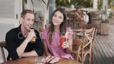 年轻夫妇在时尚的咖啡馆里喝新鲜果汁，看着相机微笑