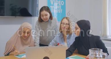 四个自信的、开朗的、多样化的同事办公室女人hija讨论商业计划使用笔记本电脑笑快乐