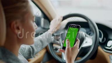 女人在车上用绿屏手机的肖像。 女人拿着智能手机