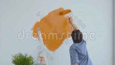 平面改造概念。 快乐的中年妇女用<strong>油漆</strong>滚筒画白色的墙，橙色的<strong>油漆</strong>
