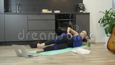女人在家里用笔记本电脑上的应用程序在健身垫上做在线有氧运动。 在家杜丽在线体育女孩培训