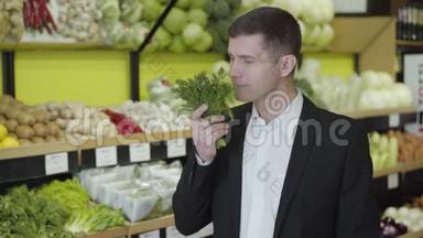 一幅白人男子微笑的肖像，闻着杂货店里新鲜的绿色植物。 穿西装的年轻人选择迪尔