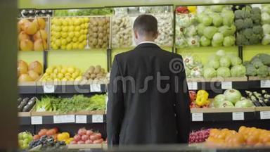 穿着西装的白种人年轻男子从货架上看着杂货店里的水果和蔬菜