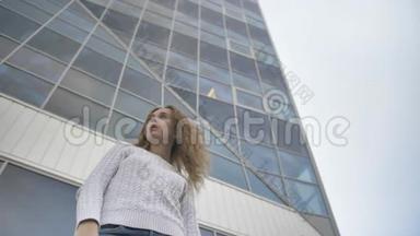 一个穿着白色毛衣、神情悲伤的女孩站在一栋商业大楼的背景上