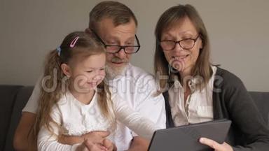 小女孩和祖父母坐在一起玩平板电脑。 孩子玩高级男女快乐