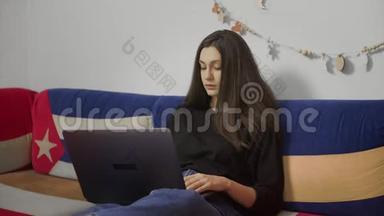 年轻的自由职业者在笔记本电脑上工作，坐在舒适的沙发上。 在家工作的自由职业者