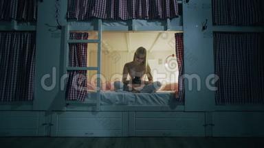 年轻漂亮的女人坐在宿舍的床上，晚上用智能手机
