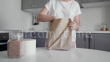 女人在木桌上打开厨房里的面包、牛奶和橘子的购物袋。 <strong>零废物</strong>之家和生态袋