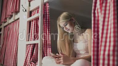 年轻漂亮的女人坐在宿舍的床上，用智能手机