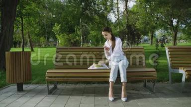 在夏天的公园里，年轻的女人坐在长凳上，手里拿着装满水果和蔬菜的棉网购物袋。 <strong>零废物</strong>