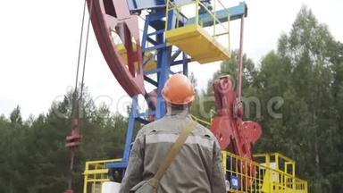 油田技术工人站在原油泵机组前.. 工程师在橙色头盔监督现场原油