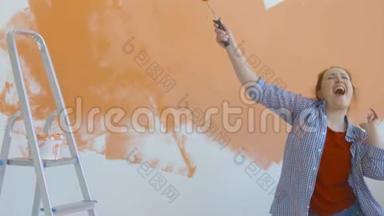 单身生活方式概念。 年轻快乐的女人用滚筒把墙壁涂成橙色