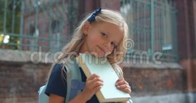 可爱的<strong>小女生</strong>拿着书看着镜头的肖像。 一头金色长发的可爱孩子