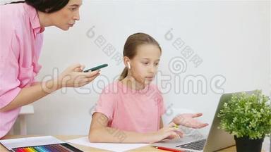 小女孩在家里电脑学习。 母亲帮助女儿完成任务。 在线培训。 儿童学习