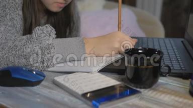 一个十几岁的女孩在家上学。 女孩在<strong>计算器</strong>上计算一个<strong>数字</strong>，并将结果写在笔记本上，特写。