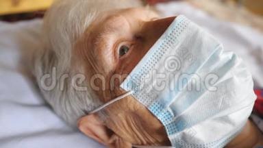 奶奶戴<strong>着</strong>医用防护口罩的病毒肖像。 可怜的女士<strong>躺着看着</strong>摄像机