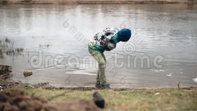 一个男孩把河岸上的石头扔进水里。 沿着河岸散步
