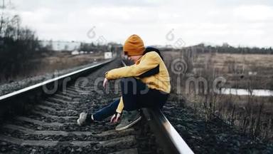 一个孤独的男孩坐在铁轨上，把鹅卵石向前扔。 宁静气氛