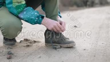 男孩把鞋带系在运动鞋上。沙尘飞扬。土路