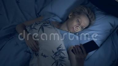 患有<strong>失眠</strong>症的女人在黑暗中躺在床上使用智能手机