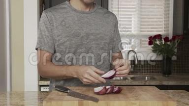 年轻的帅哥在一把大菜刀旁边的木板上的桌子上清理厨房里的红洋葱