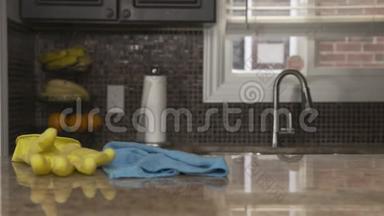 一个穿灰色T恤的年轻人在他家打扫厨房花岗岩台面。 他戴着一只亮黄色的橡胶手套