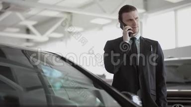 年轻人在打电话，站在汽车沙龙里，男人在打电话，交流，微笑。 他正在选车
