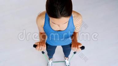 穿运动服的强壮漂亮的女孩用橡胶<strong>扩张</strong>器做二头肌运动。 她在家接受生活训练
