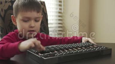 穿着红色毛衣的小学生坐在桌子旁，用旧算盘学习数学。 快乐的孩子教算盘数学