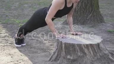 适合女人在树林里锻炼，在公园的原木上做俯卧撑。 在露天自然健身房锻炼。 俯卧撑。 吸引力