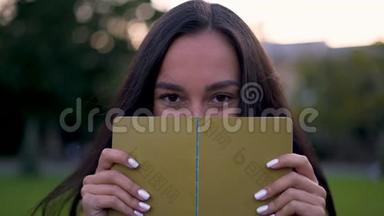 迷人的拉丁女孩神秘地用一本书遮住了她的脸。 4K