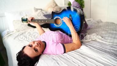 年轻女子在卧室<strong>弹吉他</strong>。 年轻女子在床上<strong>弹吉他</strong>。 她喜欢业余时间。 美丽美丽
