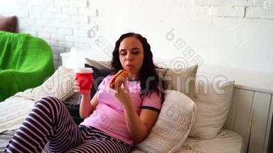 一个年轻的女人在床上<strong>吃</strong>热狗和喝咖啡。 在床上<strong>吃</strong>早餐。 把食物送到你家。 女人<strong>吃东西</strong>