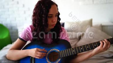年轻女子在卧室<strong>弹吉他</strong>。 年轻女子在床上<strong>弹吉他</strong>。 她喜欢业余时间。 美丽美丽