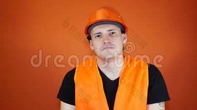 男建筑工人穿着工作服，在橙色背景下从脸上摘下医用口罩。