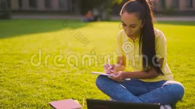 准备<strong>上课</strong>的女学生。 女孩坐在草坪上，在笔记本上记笔记。 4K
