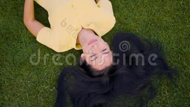 可爱的长发女孩躺在草地上享受生活。 4K