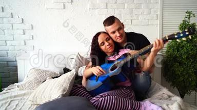 可爱的一对吉他<strong>坐在床上</strong>。 男人抱着女友<strong>坐在床上</strong>弹蓝声吉他